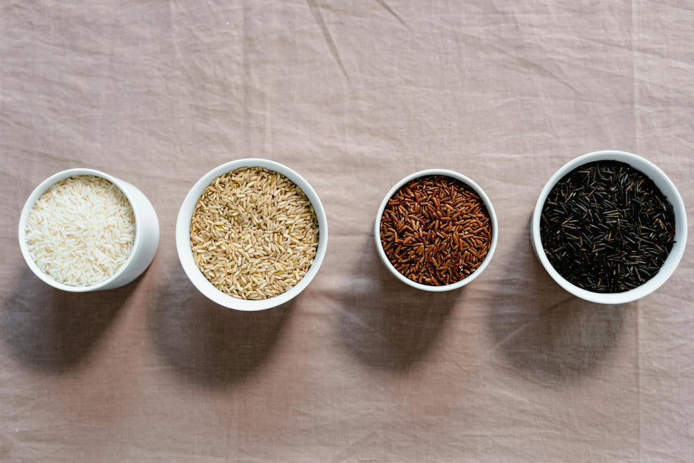 Four types of rice in bowls: white, brown, red, and black, showcasing variety for healthy diets and glucose monitoring.
